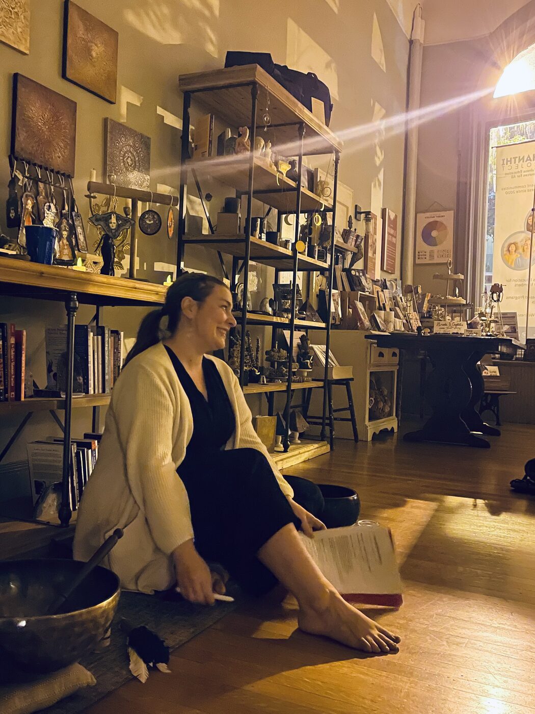 Marisa McFadden sitting on the shop floor in late afternoon light with a singing bowl and an open notebook